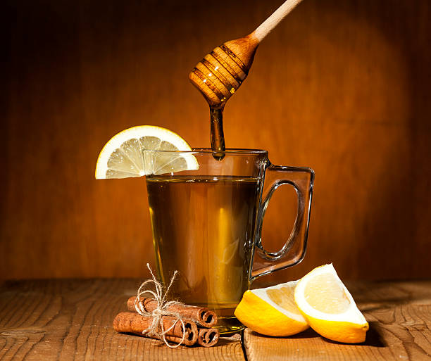 Transparent cup of tea with honey, cinnamon and lemon on wooden background.